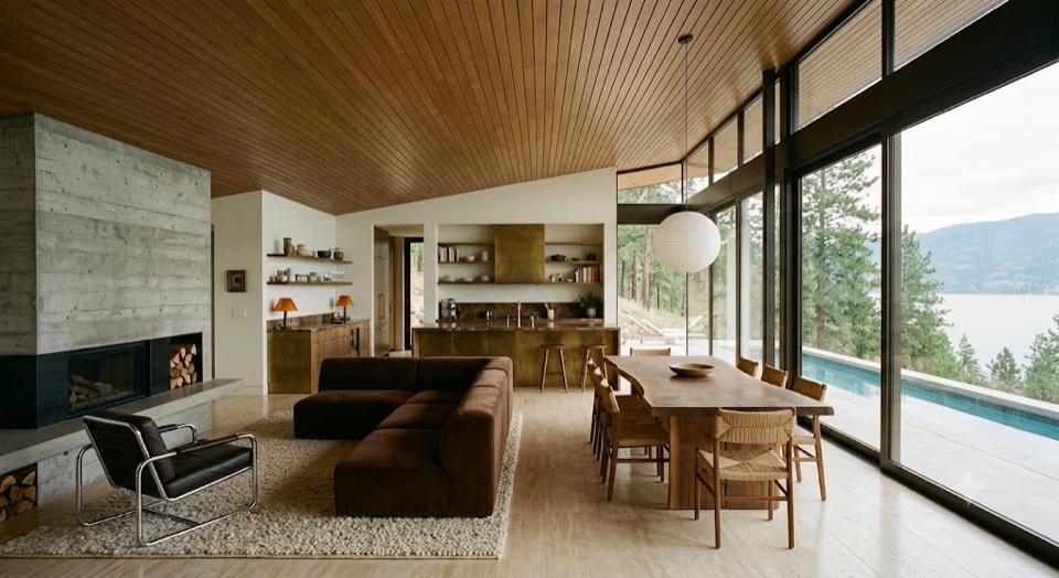 Kitchen, dining and living as one volume. Board-formed concrete hearth on the left, glass to the lake on the right.